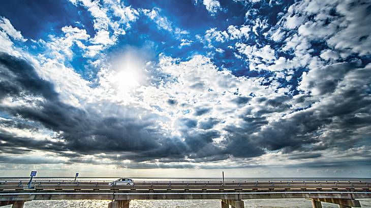 A bridge across the water with a car on it under a blue sky with clouds A bridge across the water with a car on it under a blue sky with clouds