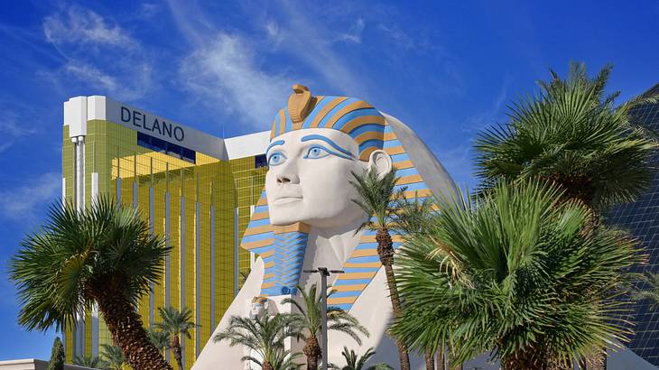 A sphinx statue with gold mirrored building behind it and palm trees surrounding it