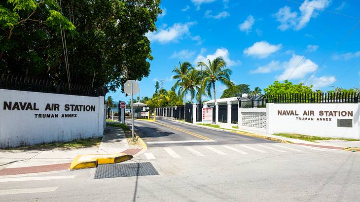 A white wall to a compound that says Naval Air Station with a road in front of it