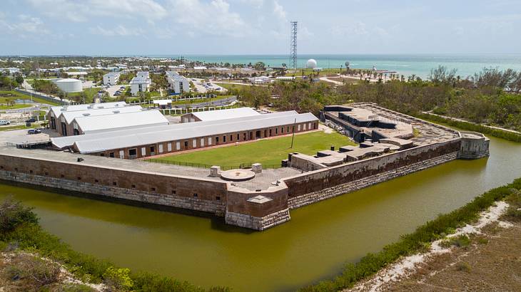 A fort with a moat and greenery surrounding it and the ocean in the distance