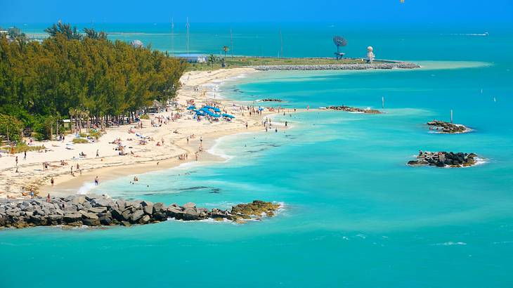 A beach with people on next to clear blue ocean and trees behind it