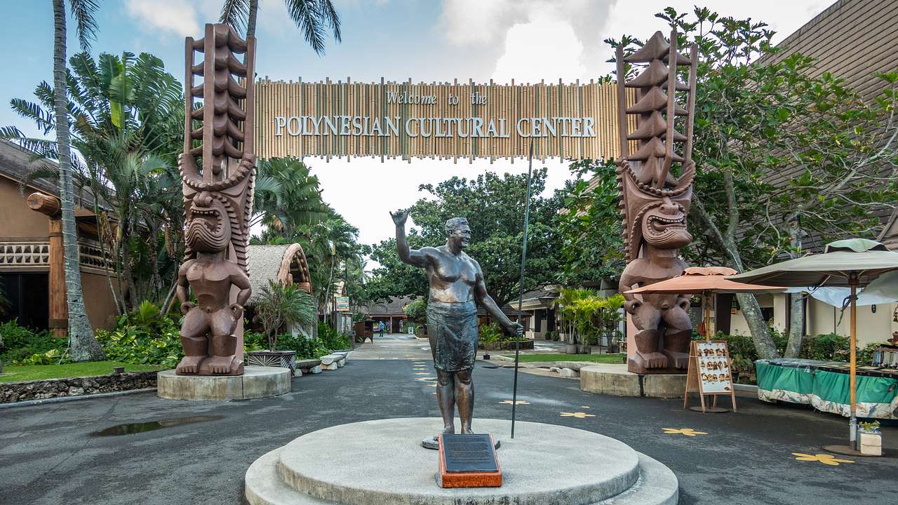 The entrance to the Polynesian Cultural Center with straw sign and statues