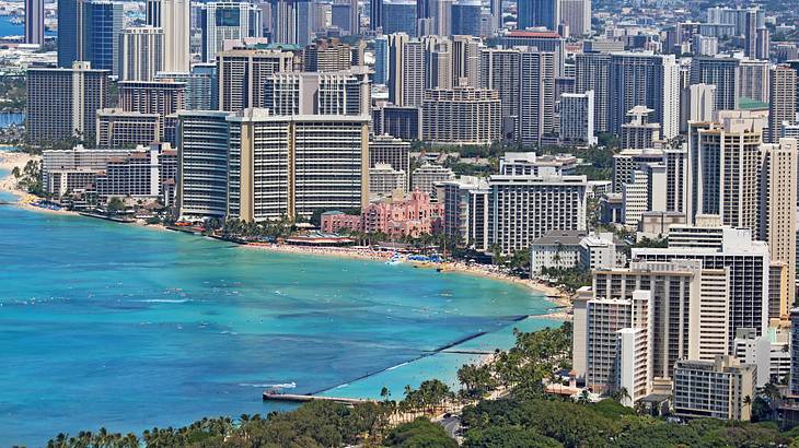 A beachside city with sand, trees, and blue ocean in front of skyscrapers