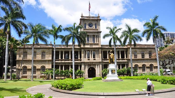 A royal palace with green grass and palm trees in front of it under a blue sky