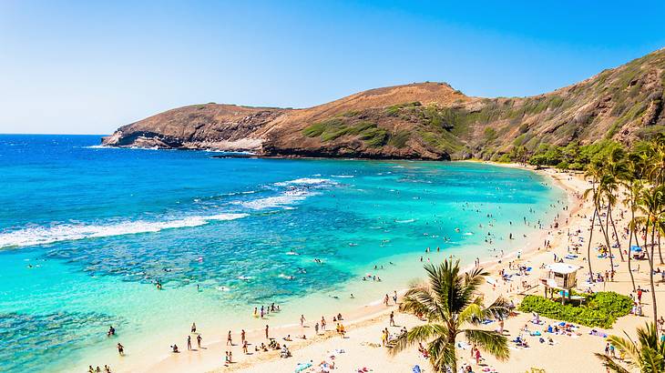 People on a sandy beach with blue ocean and mountains surrounding