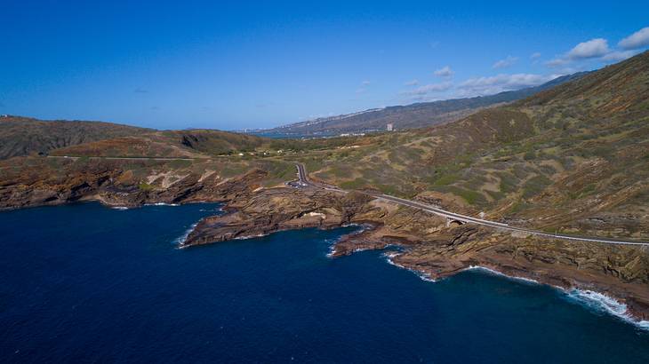 An aerial view of the ocean and greenery-covered mountains under a blue sky