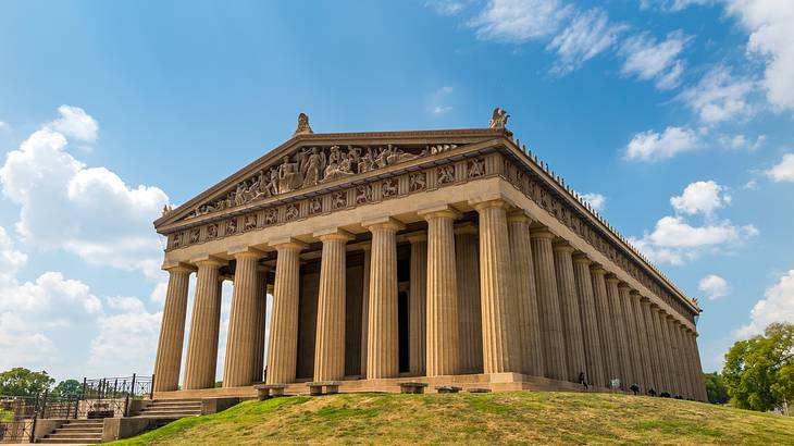 A Greek-style building with columns on a grassy hill under a blue sky