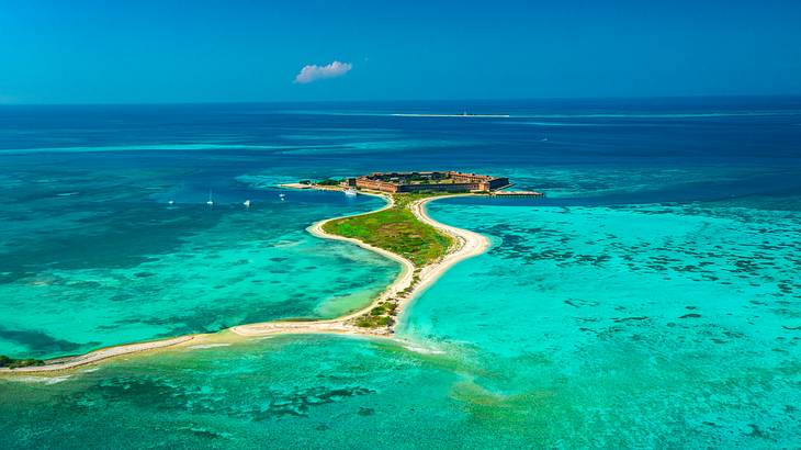 A small island with sand, greenery, and a fort on it, surrounded by the ocean