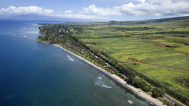 An aerial view of a coastline with green fields to the side of sand and sea