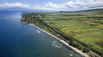 An aerial view of a coastline with green fields to the side of sand and sea