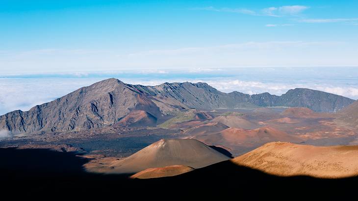 Volcanic mountain ranges with clouds surrounding them and blue sky above