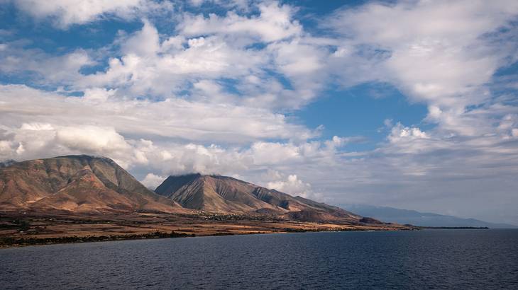 The ocean with two mountains in the background, under a blue sky with clouds