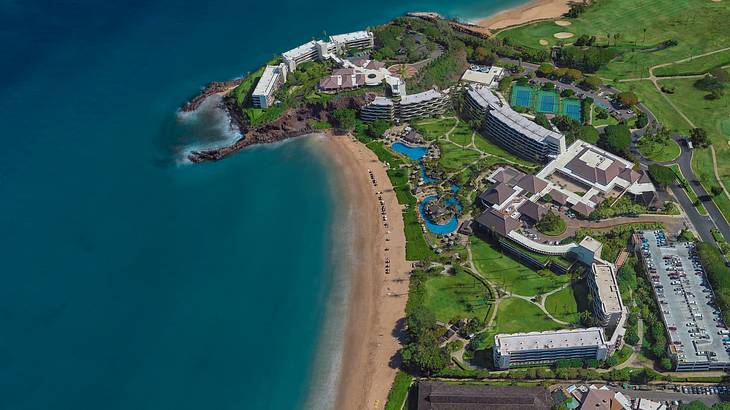 An aerial view of a coastal town with ocean, sand, greenery, and buildings