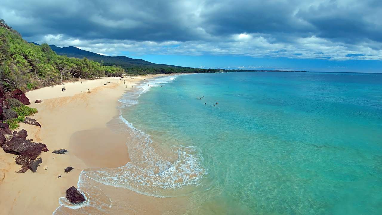 A sandy beach with turquoise ocean to one side and green mountains to the other