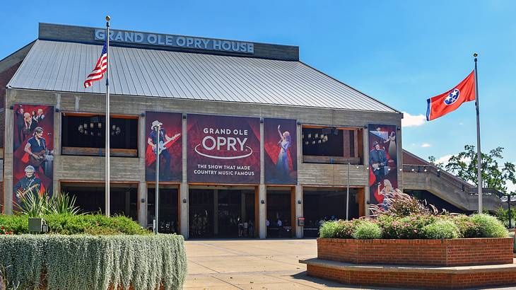 A building with Grand Ole Opry signs and flags, a path, and plants in front of it