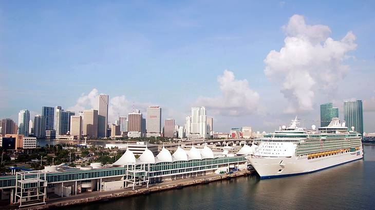 A cruise ship docked in a port with a city skyline in the background