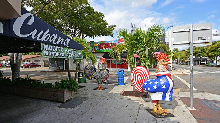 A restaurant with a "Cubana" sign and two rooster statues on the street in front