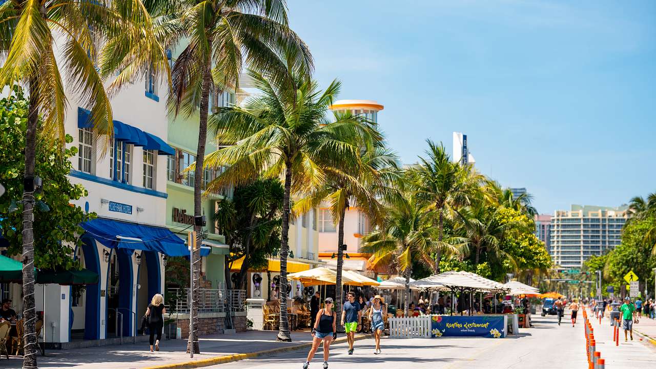 People on a street lined with pastel buildings and palm trees