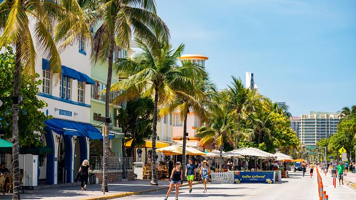 People on a street lined with pastel buildings and palm trees