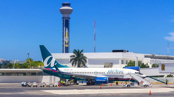 A plane on a runway with an airport, control tower, and palm trees behind it