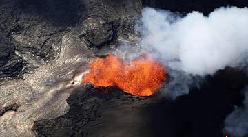 An aerial view of an active volcanic with orange lava and white smoke