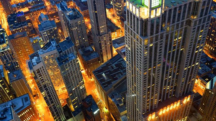 An aerial view looking down at lit-up skyscrapers and city streets at night