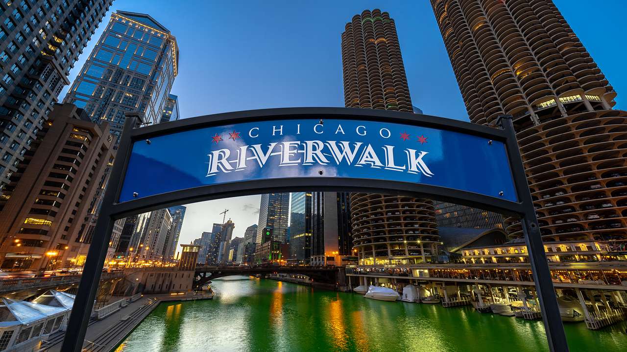 A river with skyscrapers on either side and a Chicago Riverwalk sign in front of it