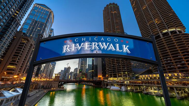 A river with skyscrapers on either side and a Chicago Riverwalk sign in front of it