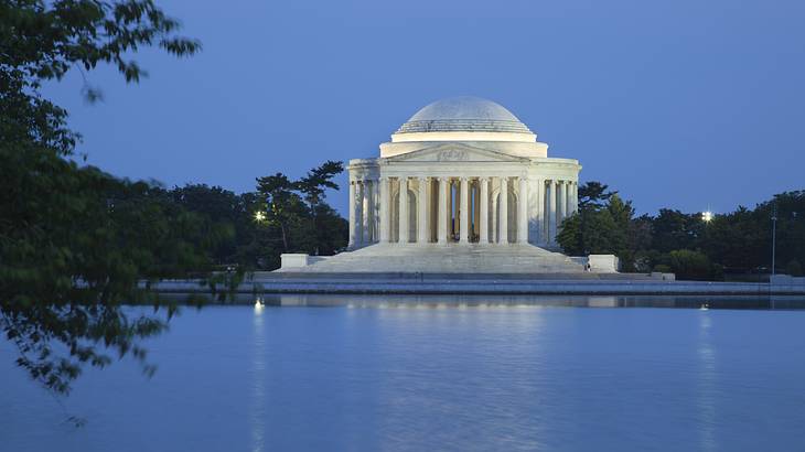 A white building with columns with water in front of it at night