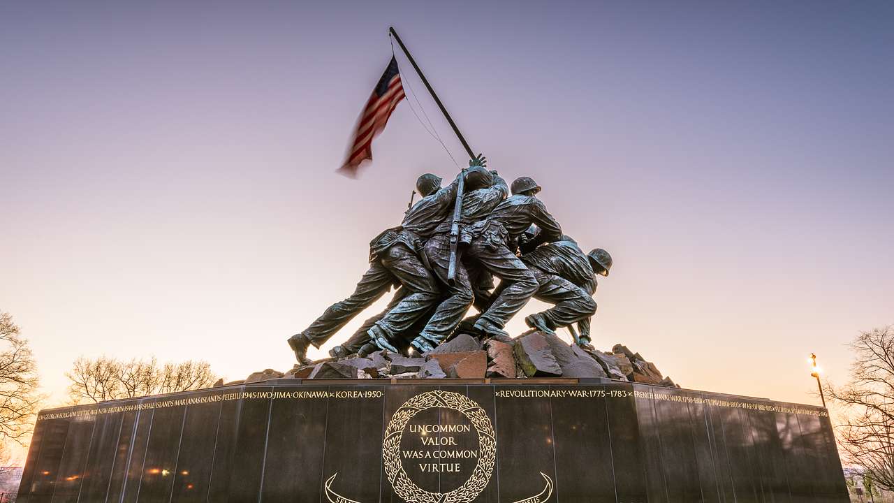 A memorial statue of soldiers pulling up a US flag at sunset