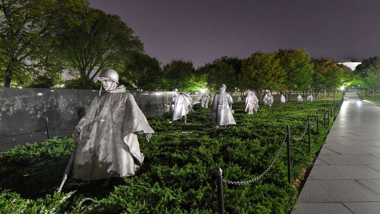 Statues of soldiers on the grass surrounded by trees and lights at night