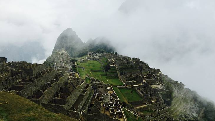 Ancient Inca ruins on a green mountain top surrounded by clouds from above