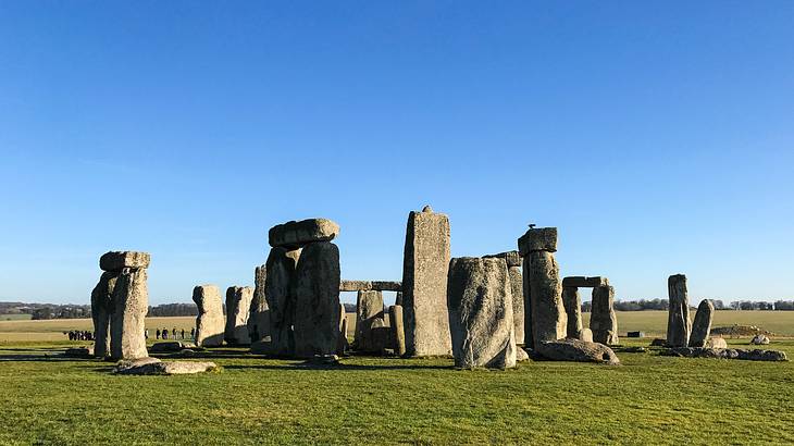 A circle of large tall stones surrounded by grass and blue sky