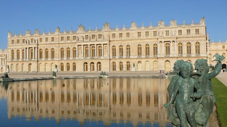 A massive palace with water and a statue in front against a blue sky