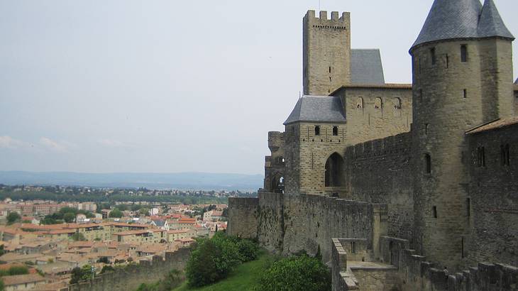 A grey castle with walls on a green hill overlooking a historic city