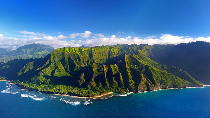 A greenery-covered mountain with ocean surrounding under a blue sky