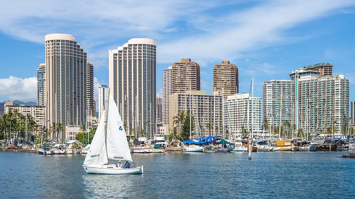 A sailboat on the water with skyscrapers and other boats behind it