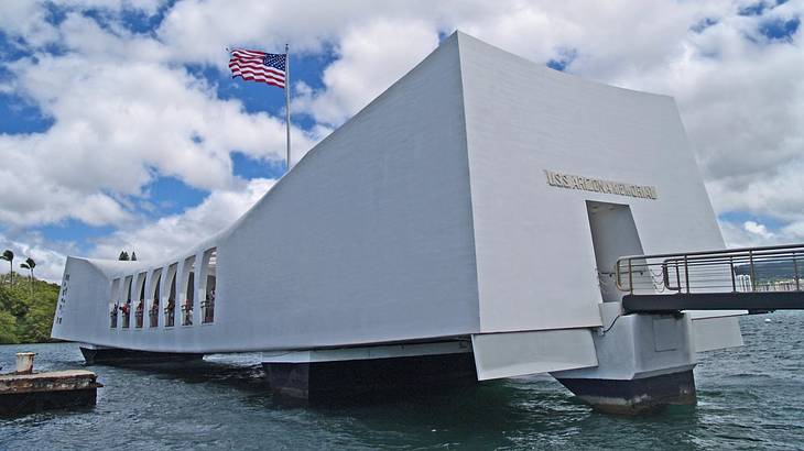 A white memorial building sitting above water with a US flag on it
