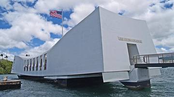 A white memorial building sitting above water with a US flag on it