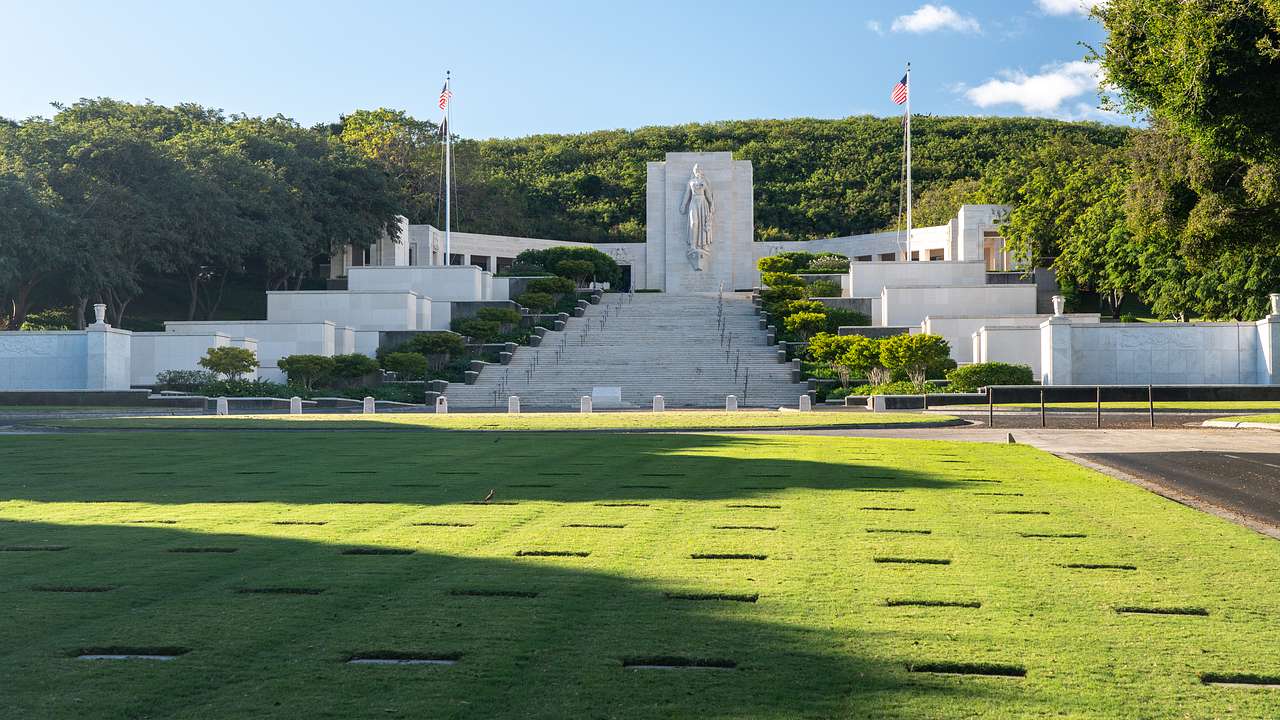 Green grass with grave markers and steps to a memorial statue in the background