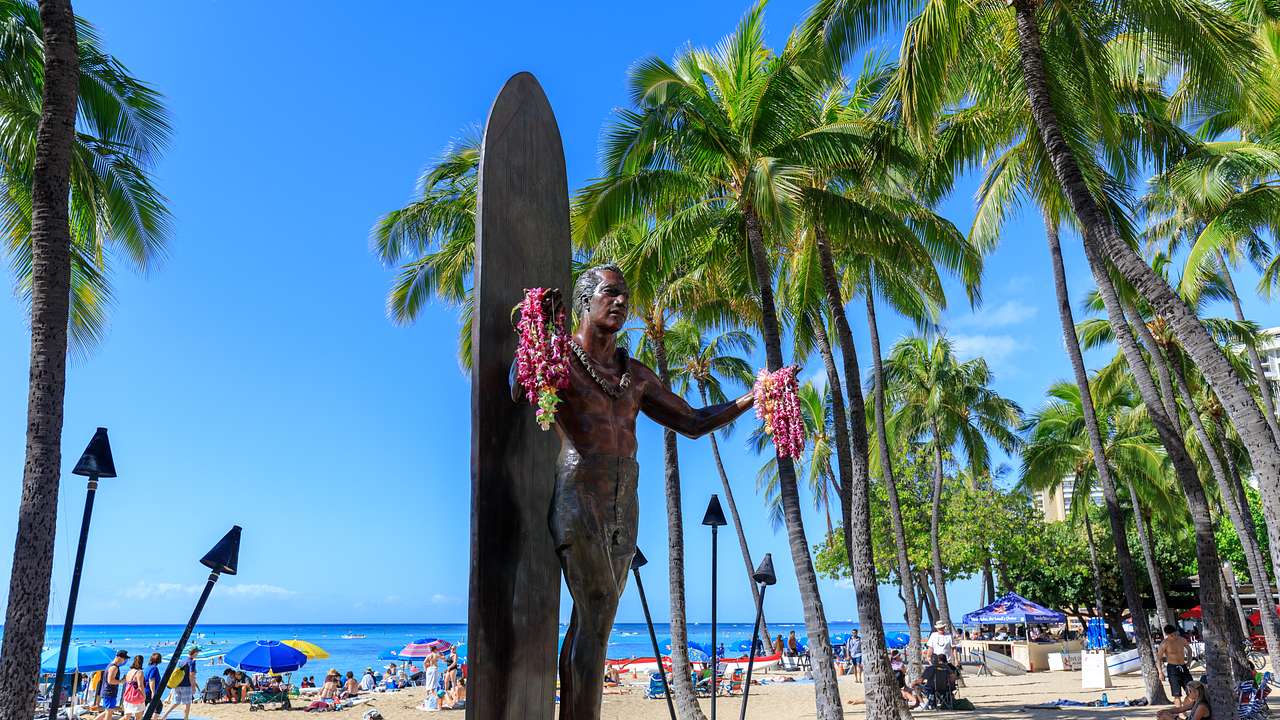 A bronze statue of a man with a surfboard behind him, holding pink flowers