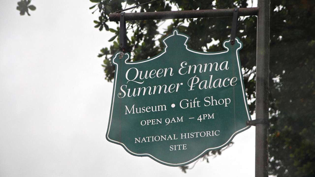 A green sign that says "Queen Emma Summer Palace" and "Museum" and "Gift Shop"