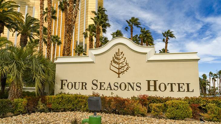 A sign that says Four Seasons Hotel with gravel in front and palm trees surrounding