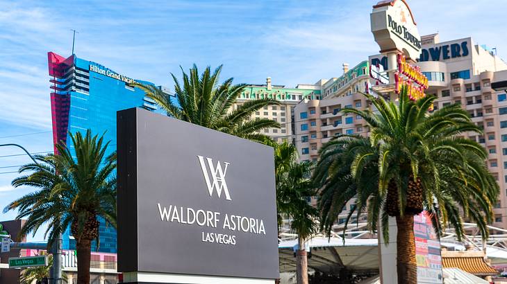 A Waldorf Astoria sign with palm trees and tall buildings behind it