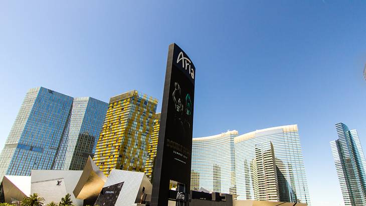 A tall black sign that says ARIA with mirrored skyscrapers behind it under blue sky