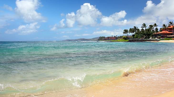 Ocean water flowing onto a sandy beach with trees and a building in the distance