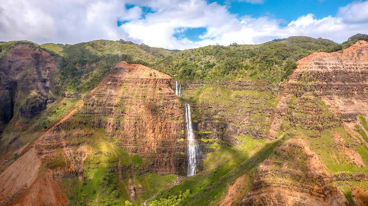 Tall mountains covered in greenery with a waterfall in the middle