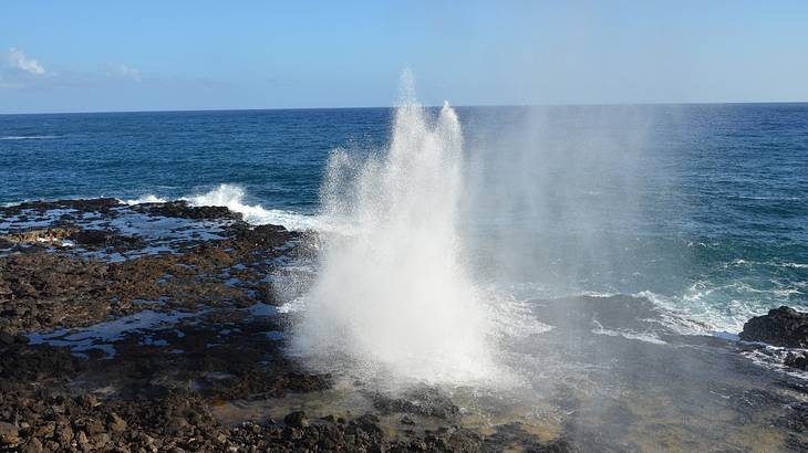 Water spraying out of volcanic rocks with the ocean in the background