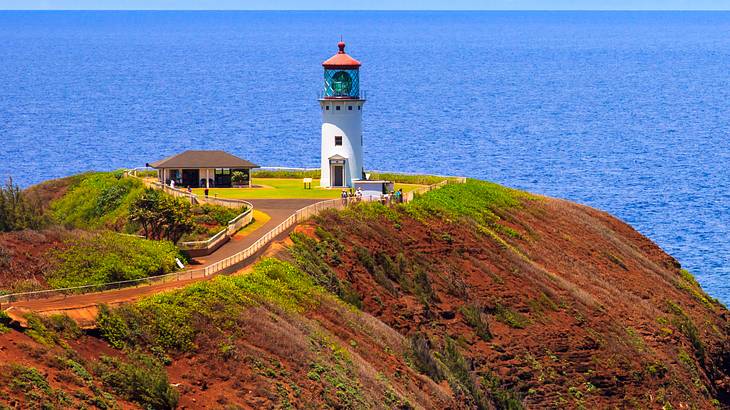 A white and red lighthouse on a cliff with the ocean behind it