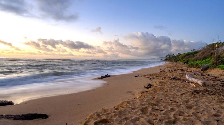 A sandy beach with ocean water flowing onto shore under a sunrise